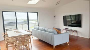 Een moderne woonkamer met een bank, eettafel, stoelen, een televisie en een plafondventilator.