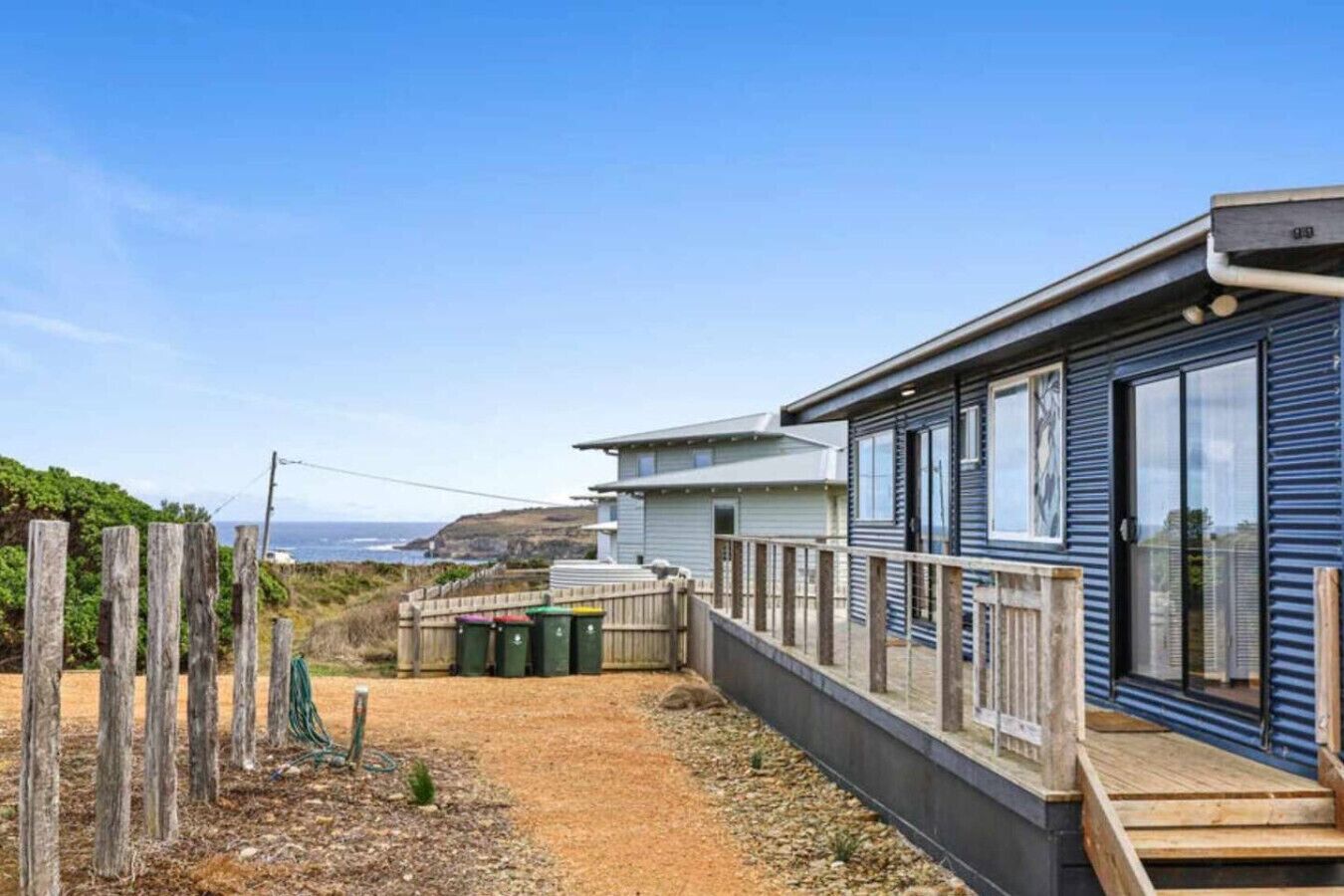 A coastal property with a wooden deck, a fenced garden, and a view of the ocean.
