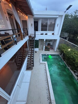 A modern two-story house with a swimming pool, a wooden staircase, and a balcony.