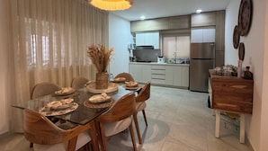 A modern dining area with a glass table, wooden chairs, and a hanging light fixture.