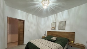 A bedroom with a bed, a wooden headboard, a nightstand, a wall-mounted shelf, and a door.