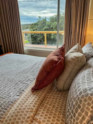 A bed with patterned bedding, a red pillow, and a view of a balcony with a railing.