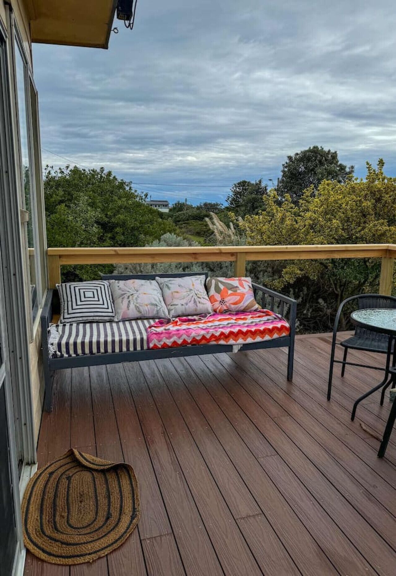 A wooden deck with a single black metal chair and a cushioned bench with pillows.