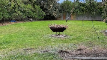 A backyard with a metal barbecue grill, a grassy lawn, and trees in the background.