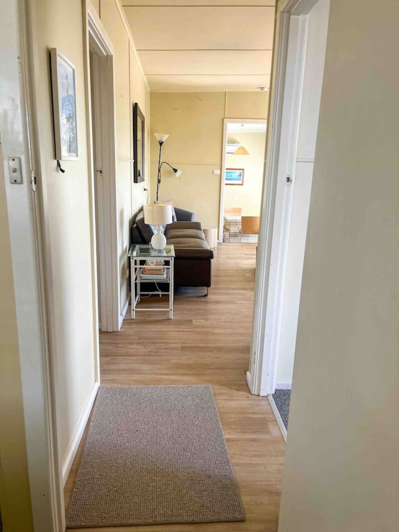 En gang der fører til et opholdsrum med en sofa, en lampe og et lille bord.