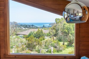 A room with a large window offering a view of a coastal landscape, including houses and trees. - Pixies at Ecobay Port Campbell (Port Campbell)