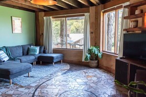A living room with a sectional sofa, a television, and a large window with curtains. - Pixies at Ecobay Port Campbell (Port Campbell)