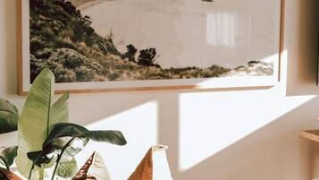 A room with a large framed artwork on the wall, a brown leather sofa, a white pillow, and a plant.