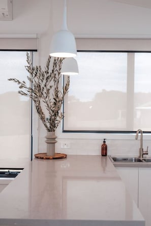 A modern kitchen with a large window, a pendant light, and a decorative plant. - Ocean Oasis Port Campbell (Port Campbell)