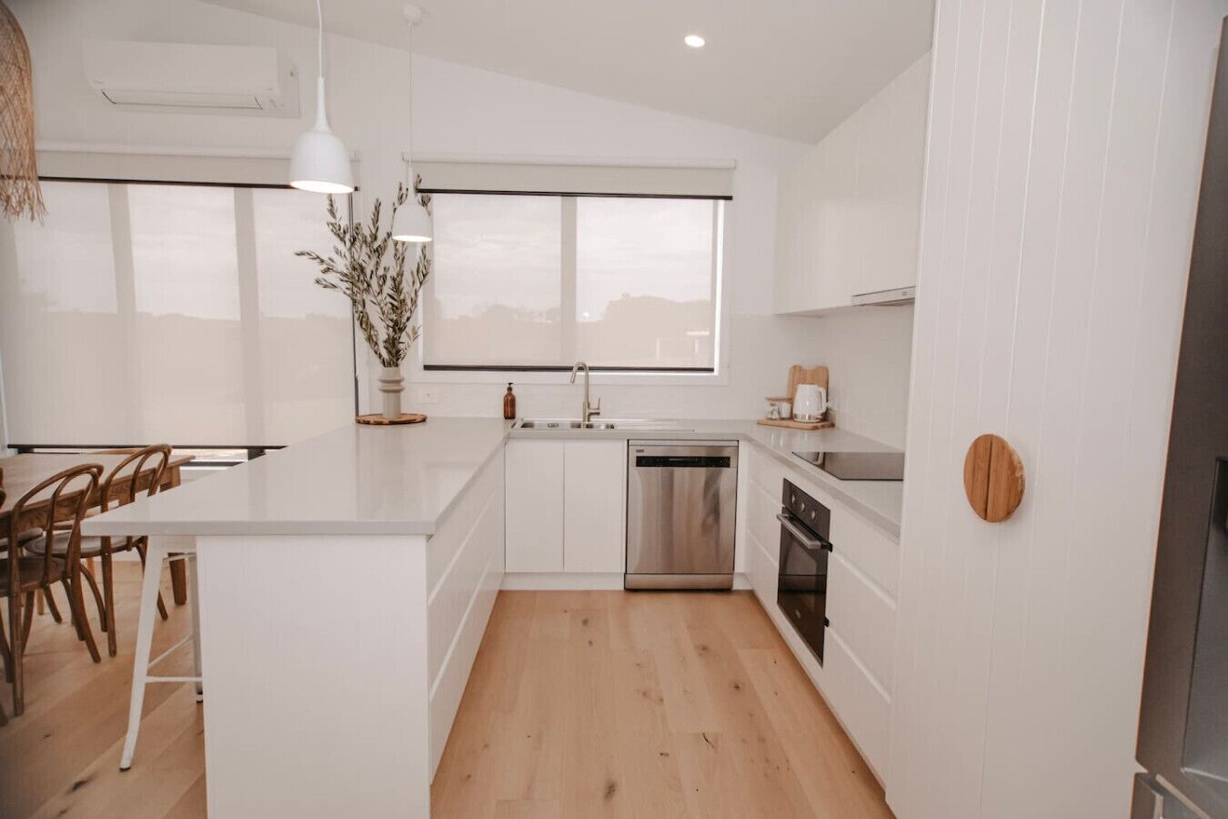A modern kitchen with white cabinetry, a central island, a built-in dishwasher, and a window above the sink.