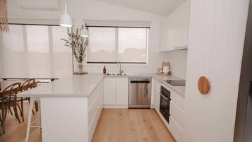 A modern kitchen with white cabinetry, a central island, a built-in dishwasher, and a window above the sink.