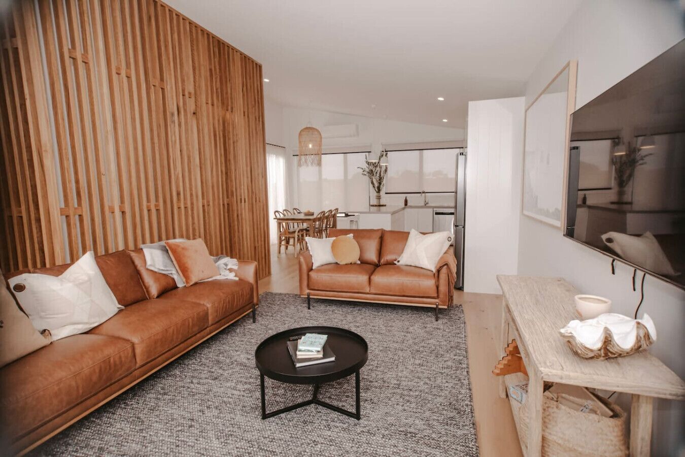 A modern living room with two leather sofas, a coffee table, and a dining area with a wooden table and chairs.