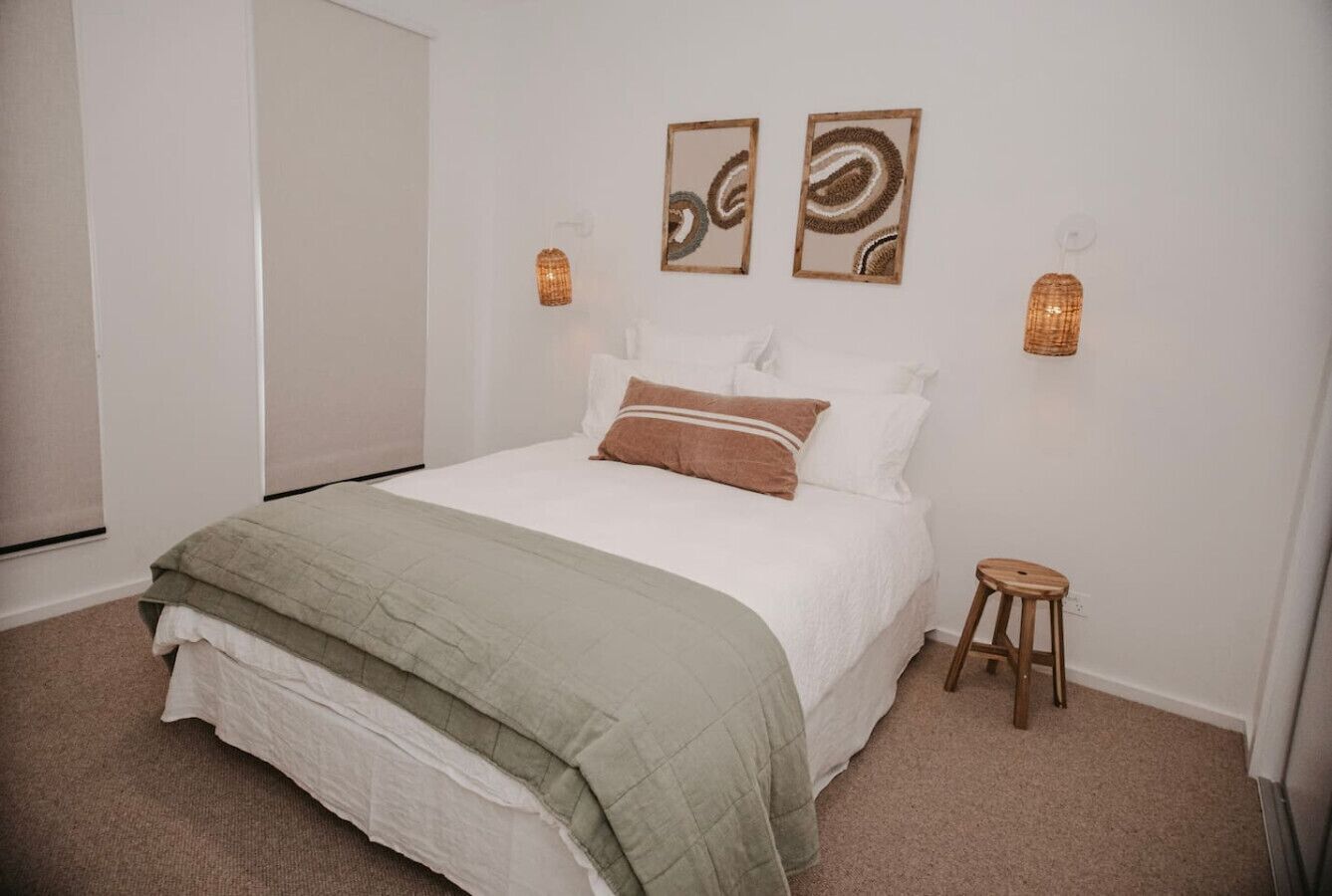 A bedroom with a bed, two wall-mounted lamps, and a small stool.