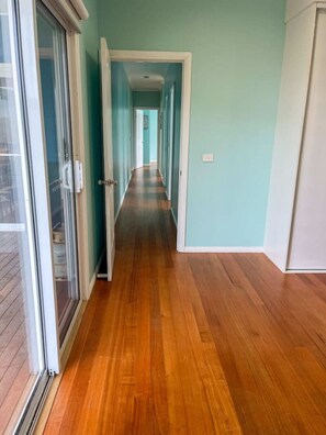 A hallway with wooden flooring, a glass door on the left, and a white door at the end. - Seabatical Port Campbell (Port Campbell)
