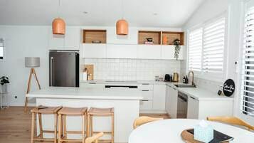 A modern kitchen with white cabinets, a central island with bar stools, pendant lighting, and a dining area with a table and chairs.