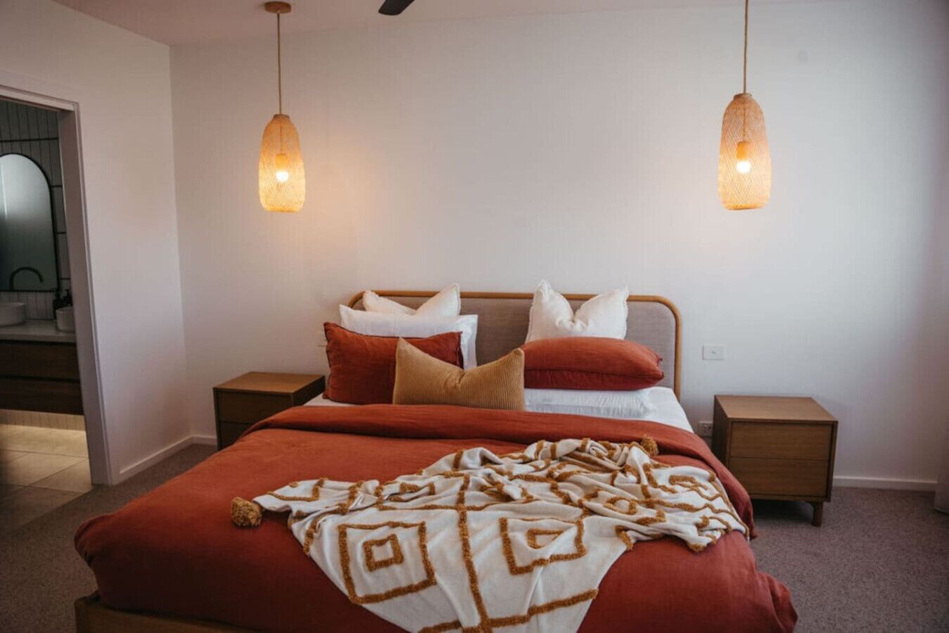 A bedroom with a bed, two bedside tables, and two hanging pendant lights.