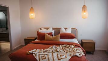A bedroom with a bed, two bedside tables, and two hanging pendant lights.