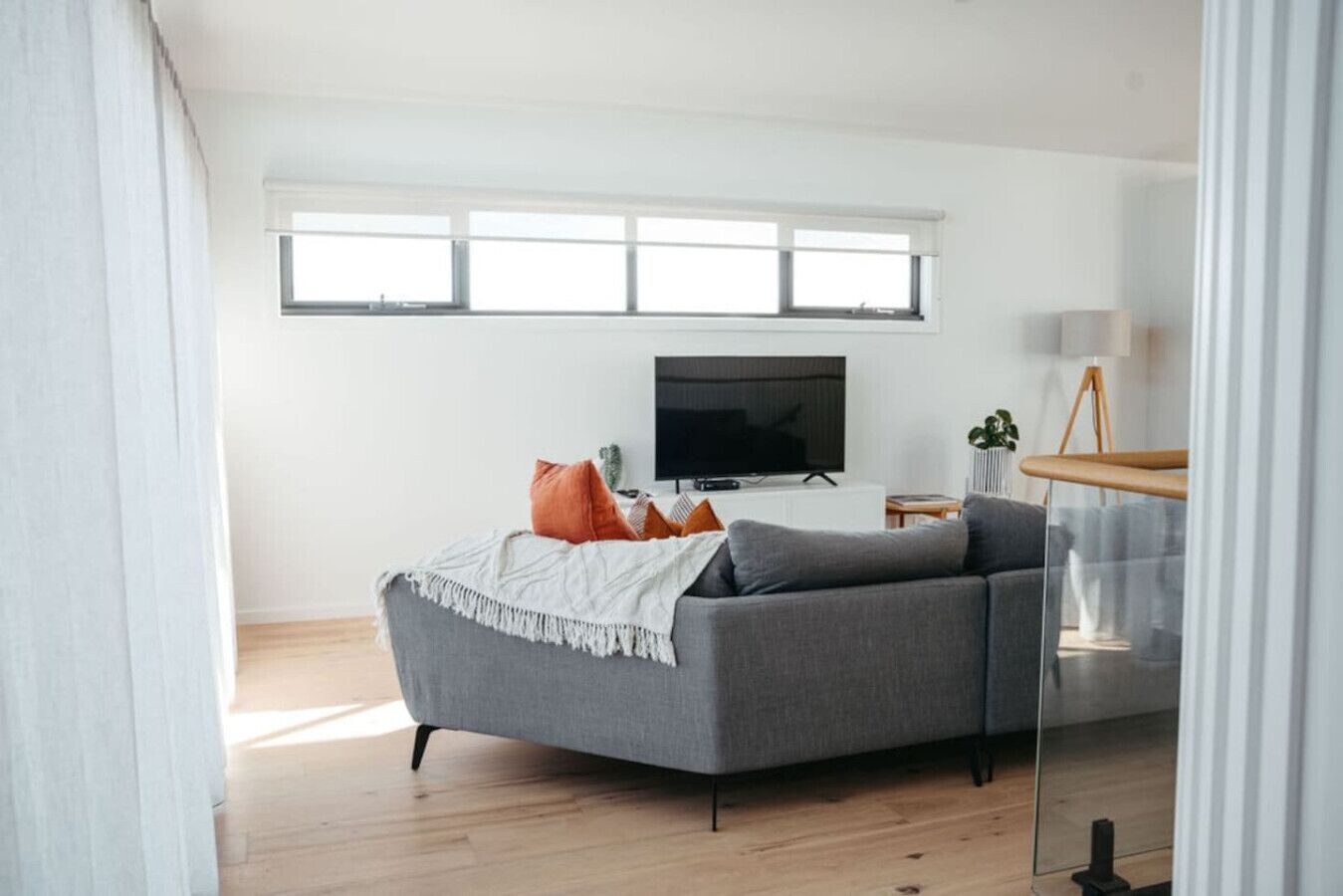 Un salon moderne avec un canapé gris, un téléviseur à écran plat et une grande fenêtre.