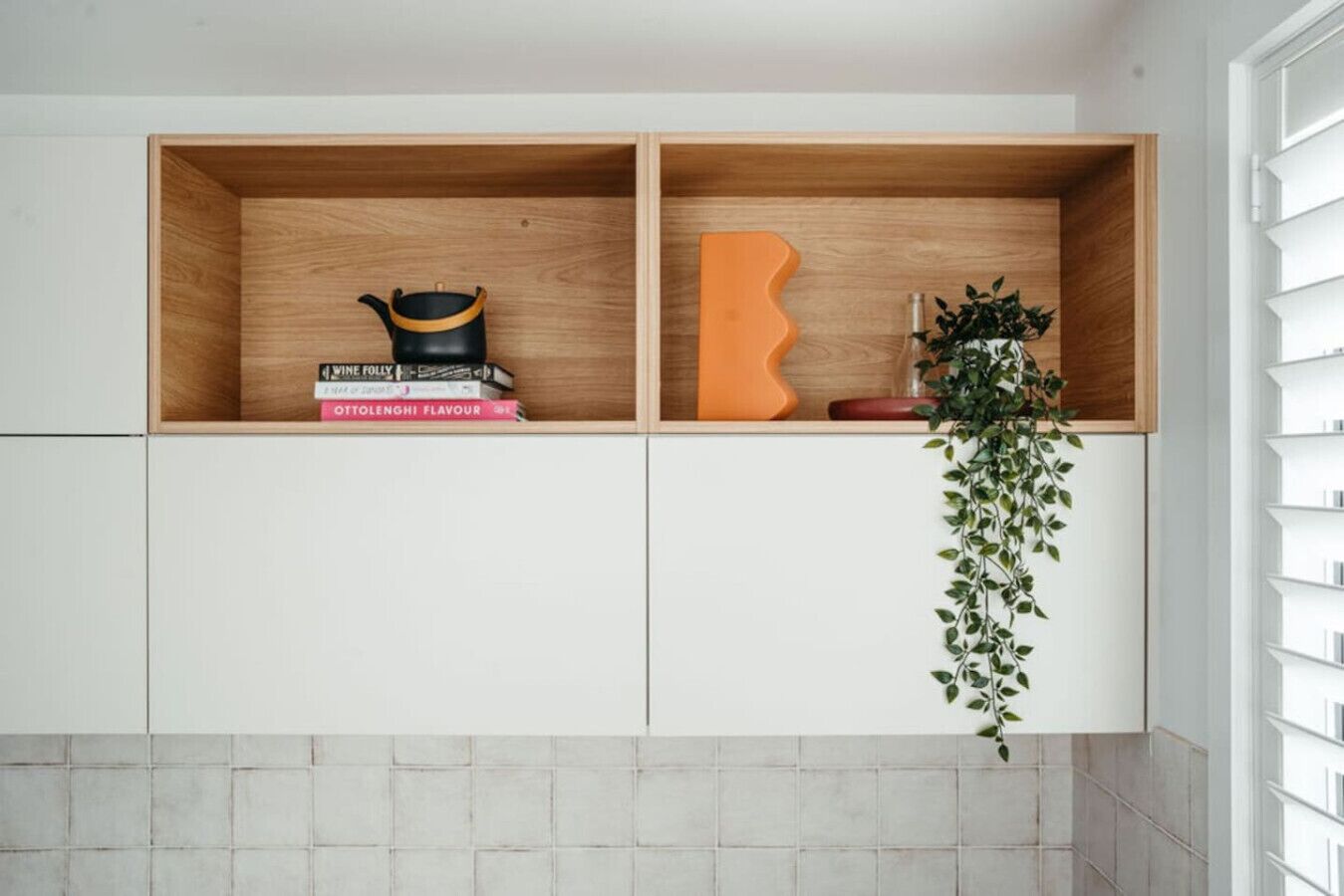 A kitchen with two wooden shelves, one containing books and a black pot, and the other with a decorative orange object and a plant.