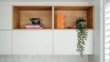 A kitchen with two wooden shelves, one containing books and a black pot, and the other with a decorative orange object and a plant.