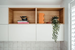 Una cocina con dos estantes de madera, uno con libros y una olla negra, y el otro con un objeto decorativo naranja y una planta.