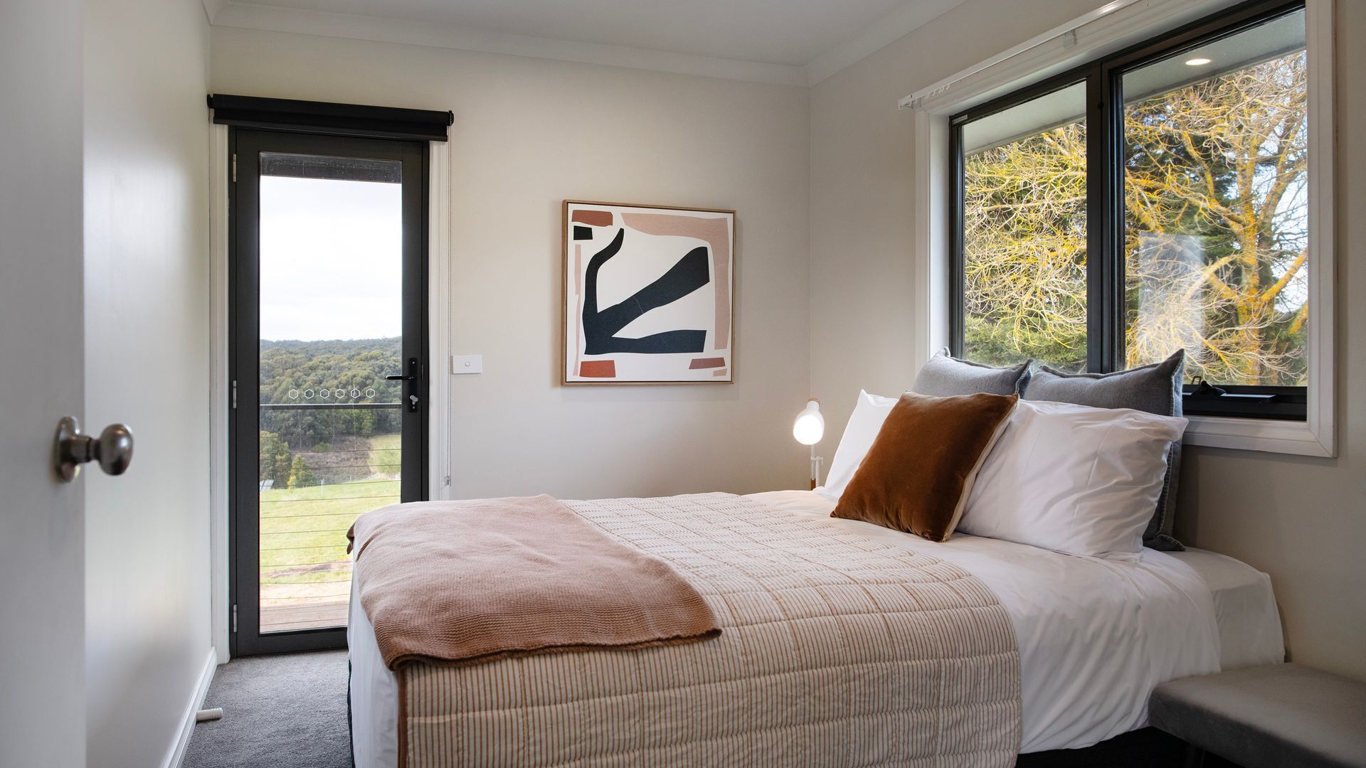 A bedroom with a bed, a window, a door, and a painting on the wall.