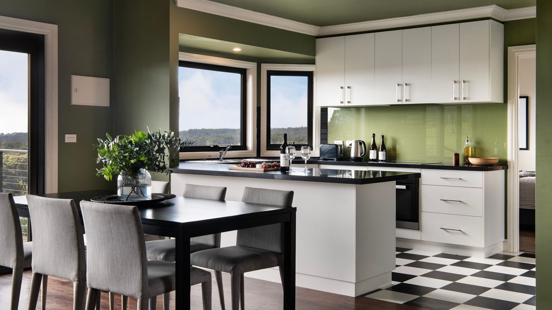A modern kitchen with a dining area, large windows, and a view of the outdoors.
