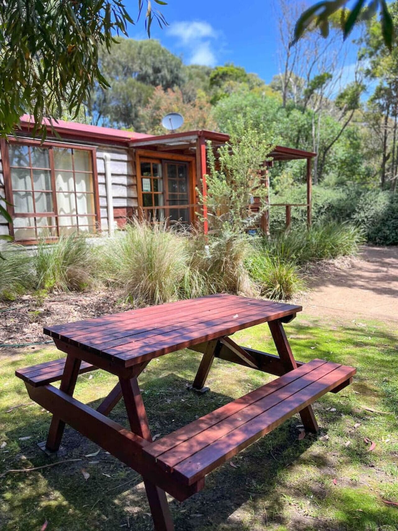 A wooden picnic table in a natural setting with a building in the background.