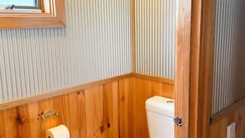 A small, compact bathroom with wooden paneling, a toilet, and a window.