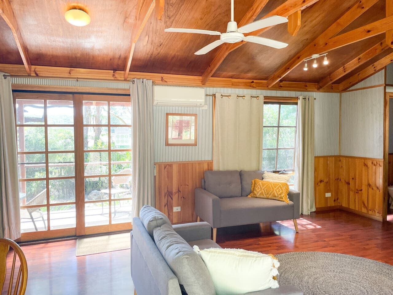 A spacious living room with a ceiling fan, a sofa, a chair, and a dining area with wooden cabinets.