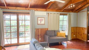 A spacious living room with a ceiling fan, a sofa, a chair, and a dining area with wooden cabinets.