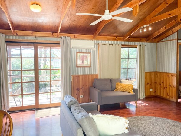 A spacious living room with a ceiling fan, a sofa, a chair, and a dining area with wooden cabinets.