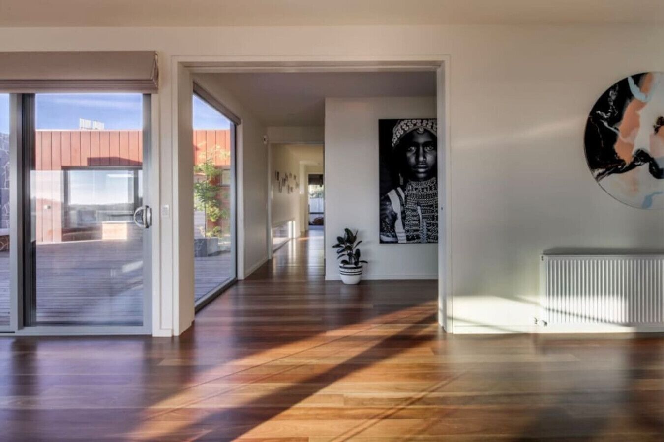 A modern interior with a wooden floor, a potted plant, and a wall-mounted artwork.