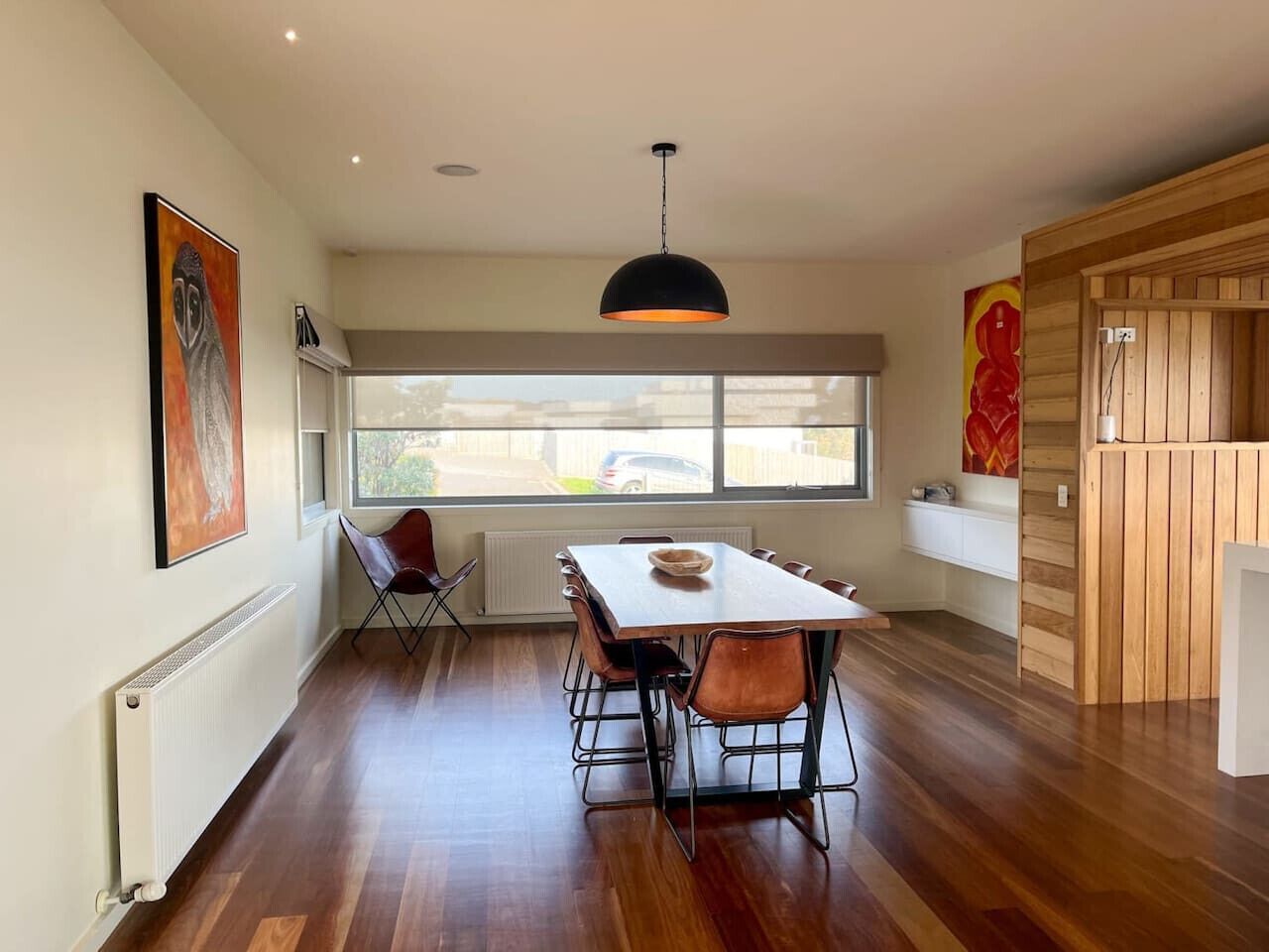 A dining area with a table and chairs, a radiator, and a window with a view of the outside.