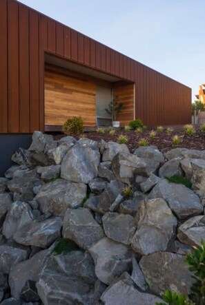 A modern building with a wooden facade, a large open entrance, and a rock garden in the foreground. - Serendipity Warrnambool (Warrnambool)