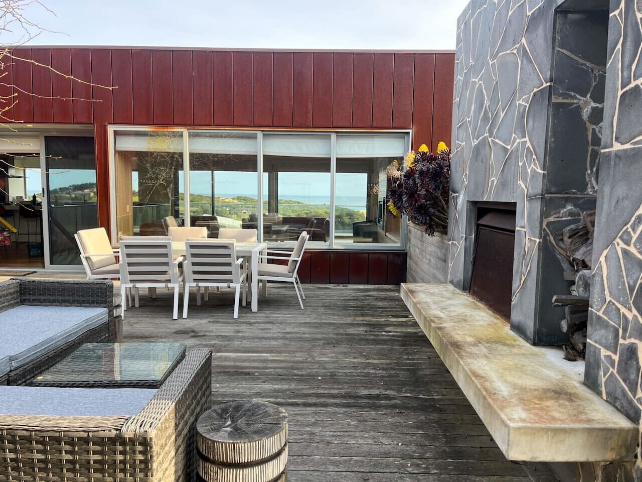 Une terrasse extérieure moderne, agrémentée d’un mur en pierre, d’un espace salon avec des chaises et une table, et offrant une vue sur le paysage.