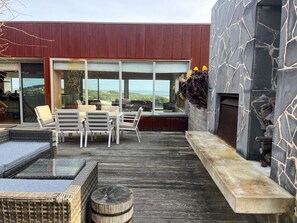 A modern outdoor deck with a stone wall, a seating area with chairs and a table, and a view of the landscape. - Serendipity Warrnambool (Warrnambool)