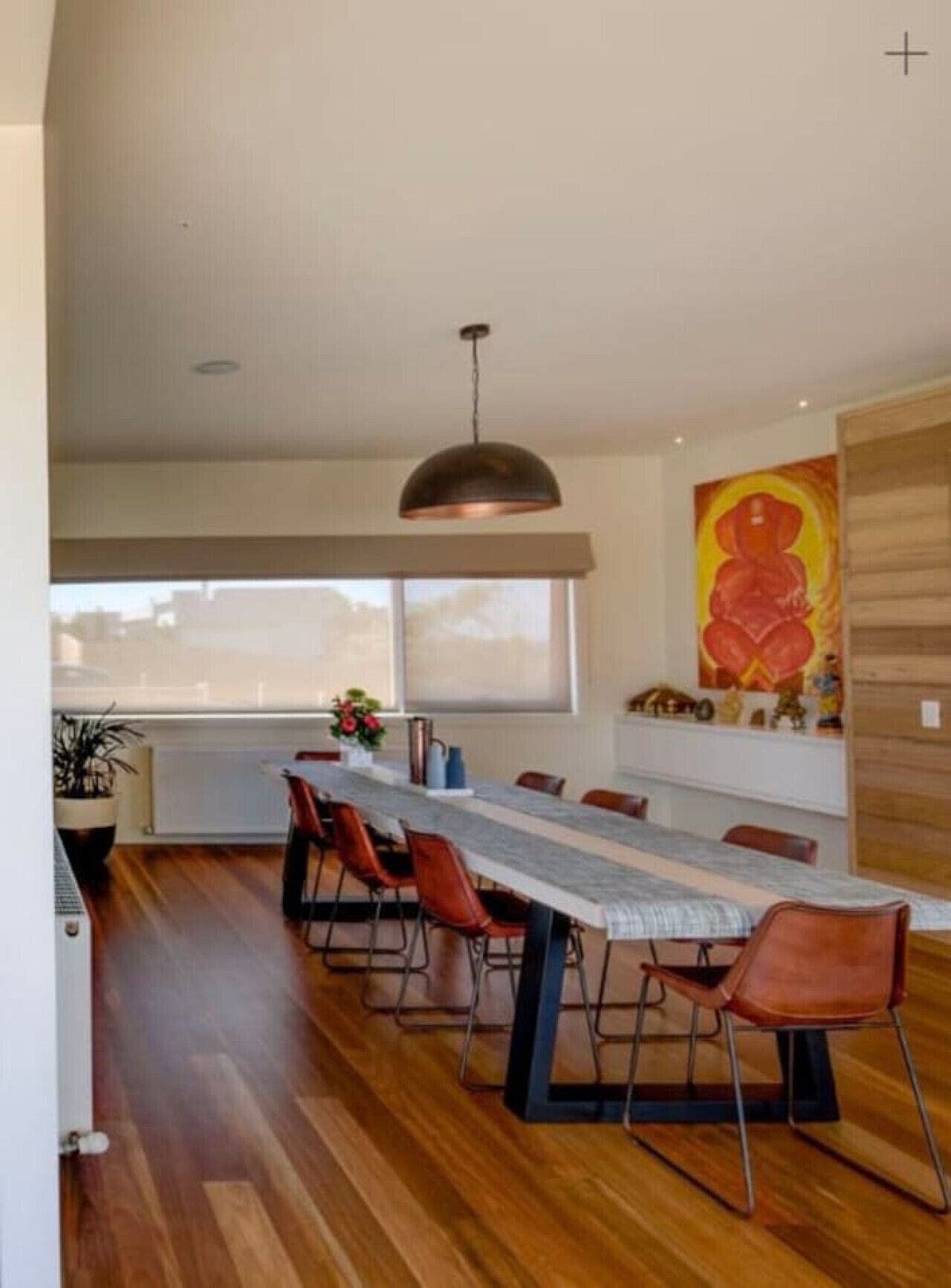 A modern dining area with a long table, red chairs, and a pendant light.