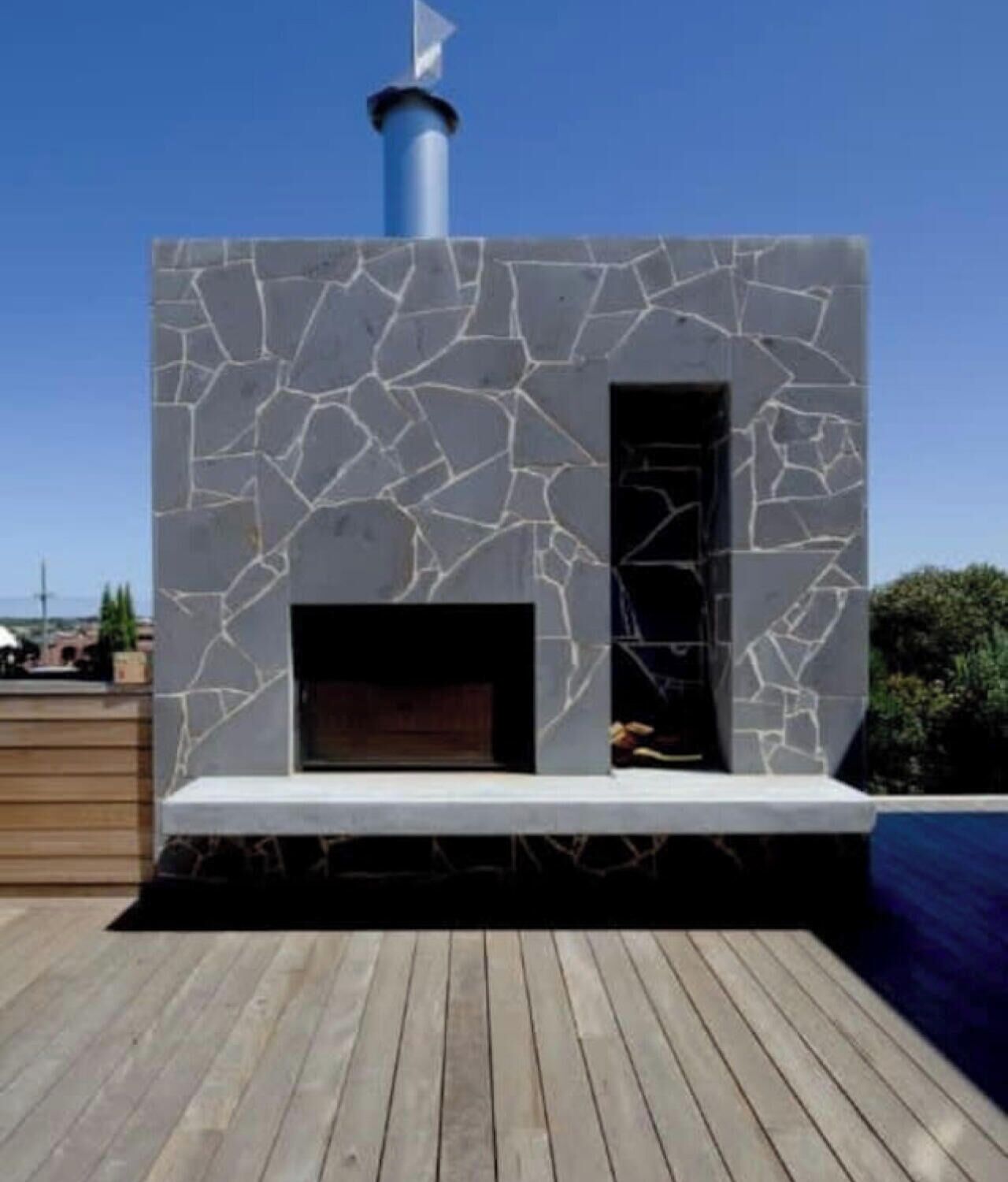 A modern outdoor fireplace with a stone facade and a chimney, situated on a wooden deck.