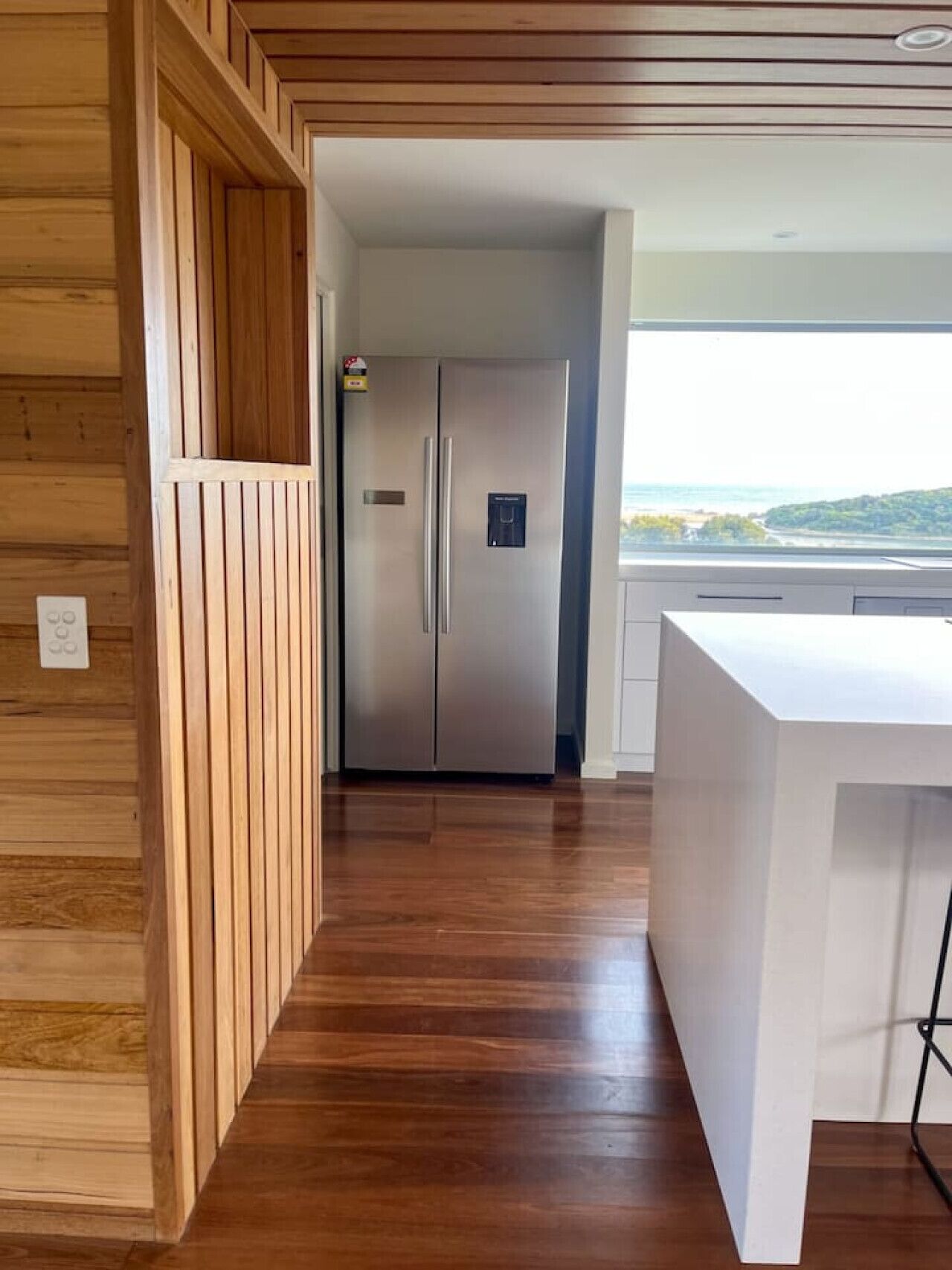 Una cocina moderna con un refrigerador de acero inoxidable, paneles de madera y vistas por la ventana.