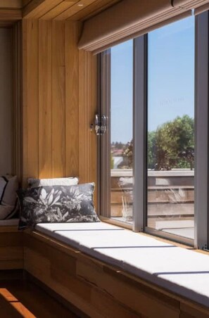 A room with a wooden paneled wall, a window seat with cushions, and a view of the outdoors.