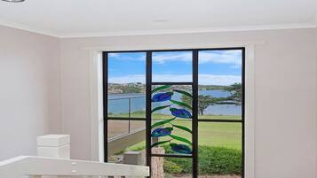 A room with a large window featuring a decorative glass design, a white railing, and a view of a lake and distant landscape.