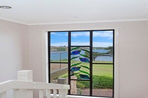 A room with a large window featuring a decorative glass design, a white railing, and a view of a lake and distant landscape.