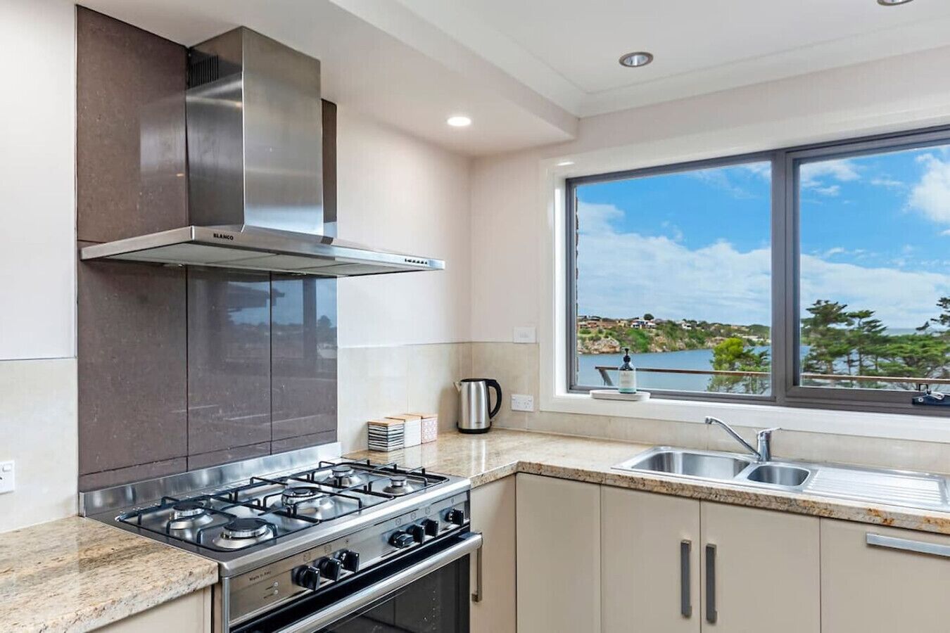 Een moderne keuken met een gasfornuis, een rvs-afzuigkap en een raam met uitzicht op een meer.