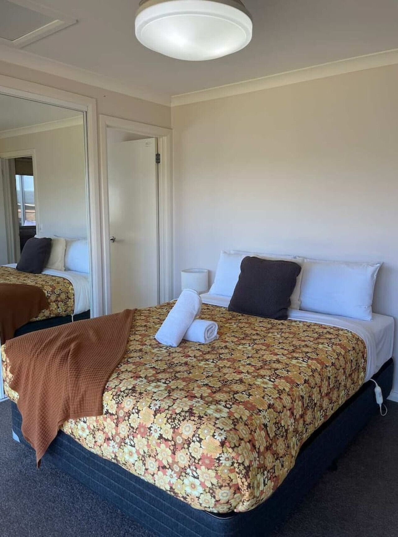 A hotel room with a double bed, a bedside table with a lamp, a mirror, and a door leading to another room.