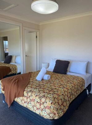 Habitación de hotel con una cama doble, una mesita de noche con lámpara, un espejo y una puerta que da a otra habitación.