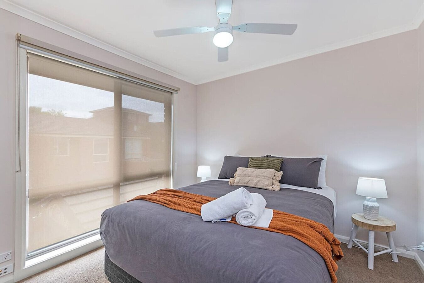 A bedroom with a bed, a ceiling fan, a nightstand, and a window with blinds.