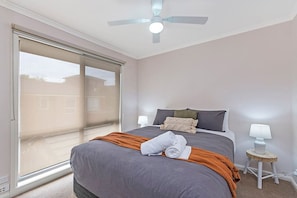 A bedroom with a bed, a ceiling fan, a nightstand, and a window with blinds.