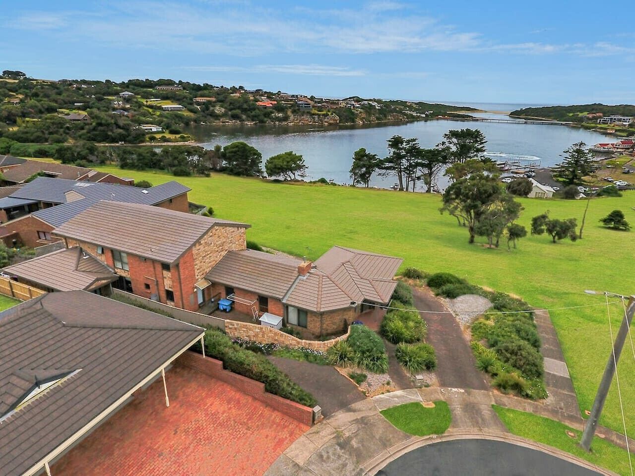 A residential area with houses, a grassy lawn, and a body of water in the background.