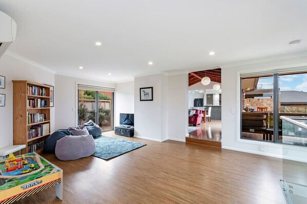 A spacious living room with a wooden floor, a bookshelf, a TV, and a large window.